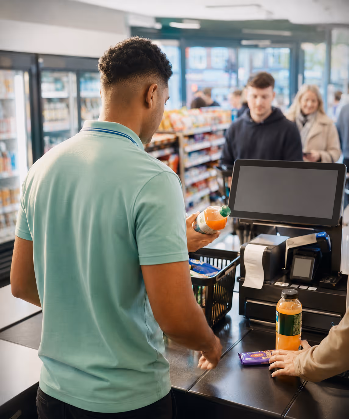 A convenience-store front counter with a customer queue, the cashier scanning items quickly on the RouteMagic POS.