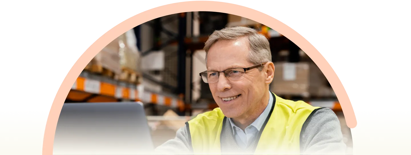 Smiling warehouse manager in a yellow safety vest standing in a modern distribution facility.
