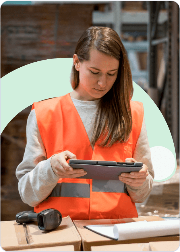 Professional warehouse worker in orange safety vest using tablet for advanced analytics and route optimization in modern logistics facility