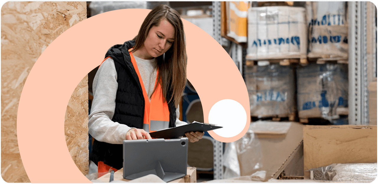 Female warehouse worker in orange safety vest using tablet for digital inventory management in modern distribution center